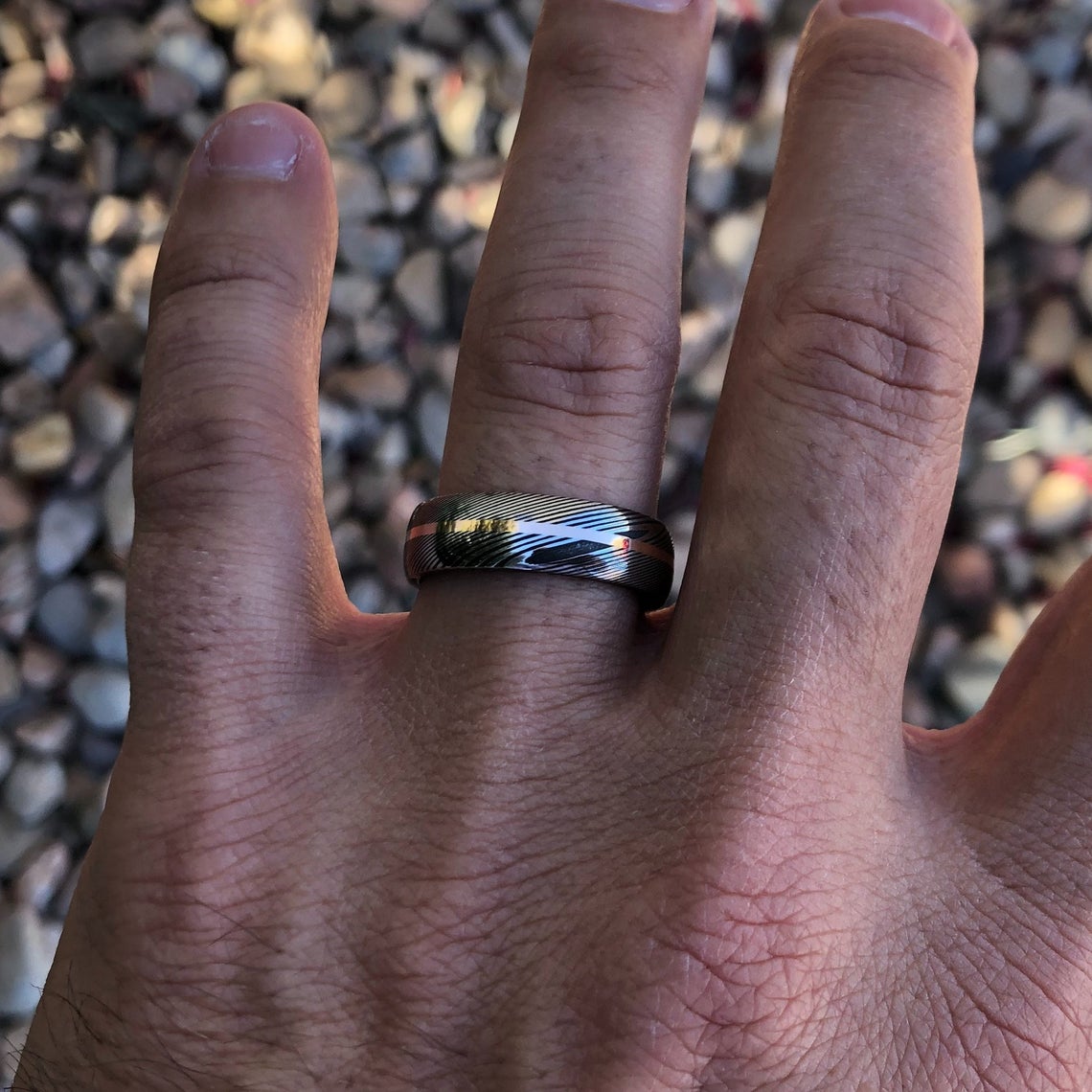 7mm wide Damascus steel ring with a centered rose gold inlay on a man&#39;s hand
