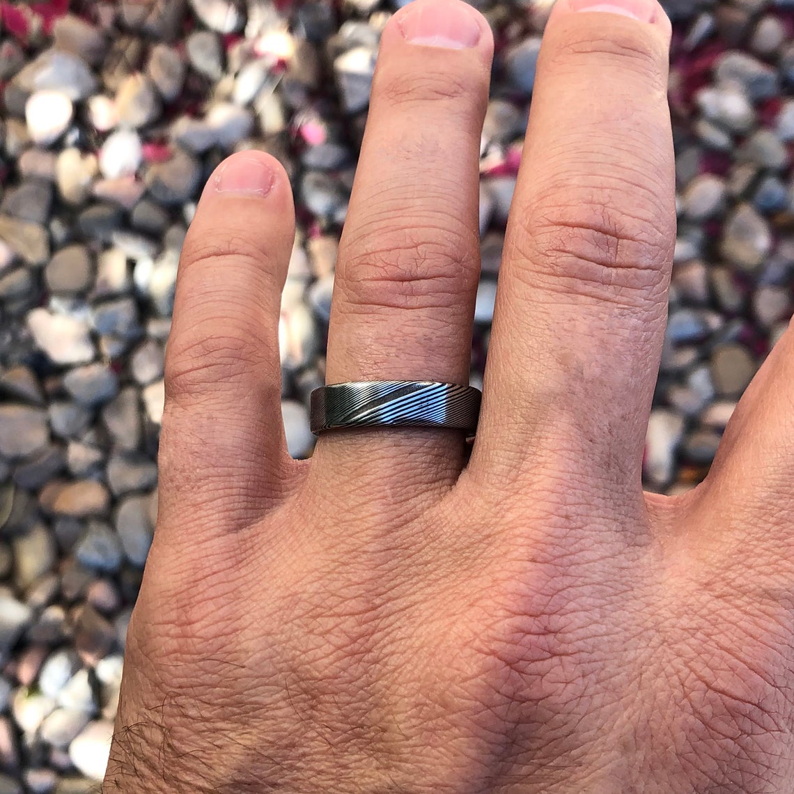 6mm wide Damascus steel wedding band with a flat profile on a man&#39;s hand