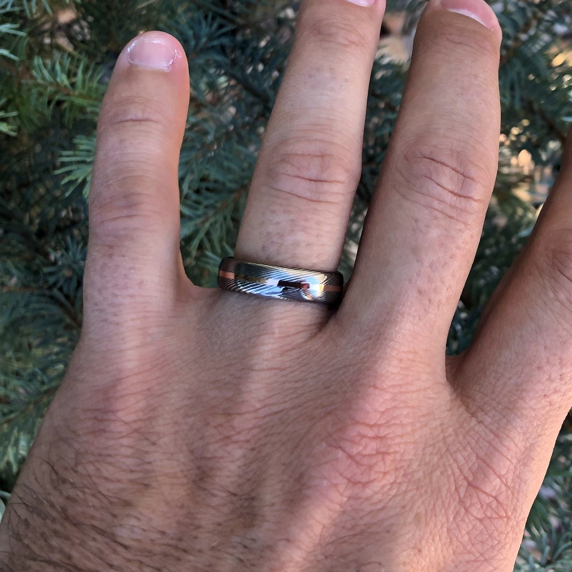 6mm wide Damascus steel ring with a centered rose gold inlay and a rounded profile on a man&#39;s hand