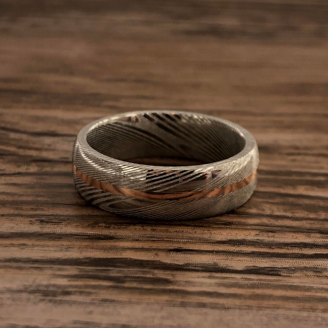 7mm wide white Damascus steel ring with a centered rose gold inlay