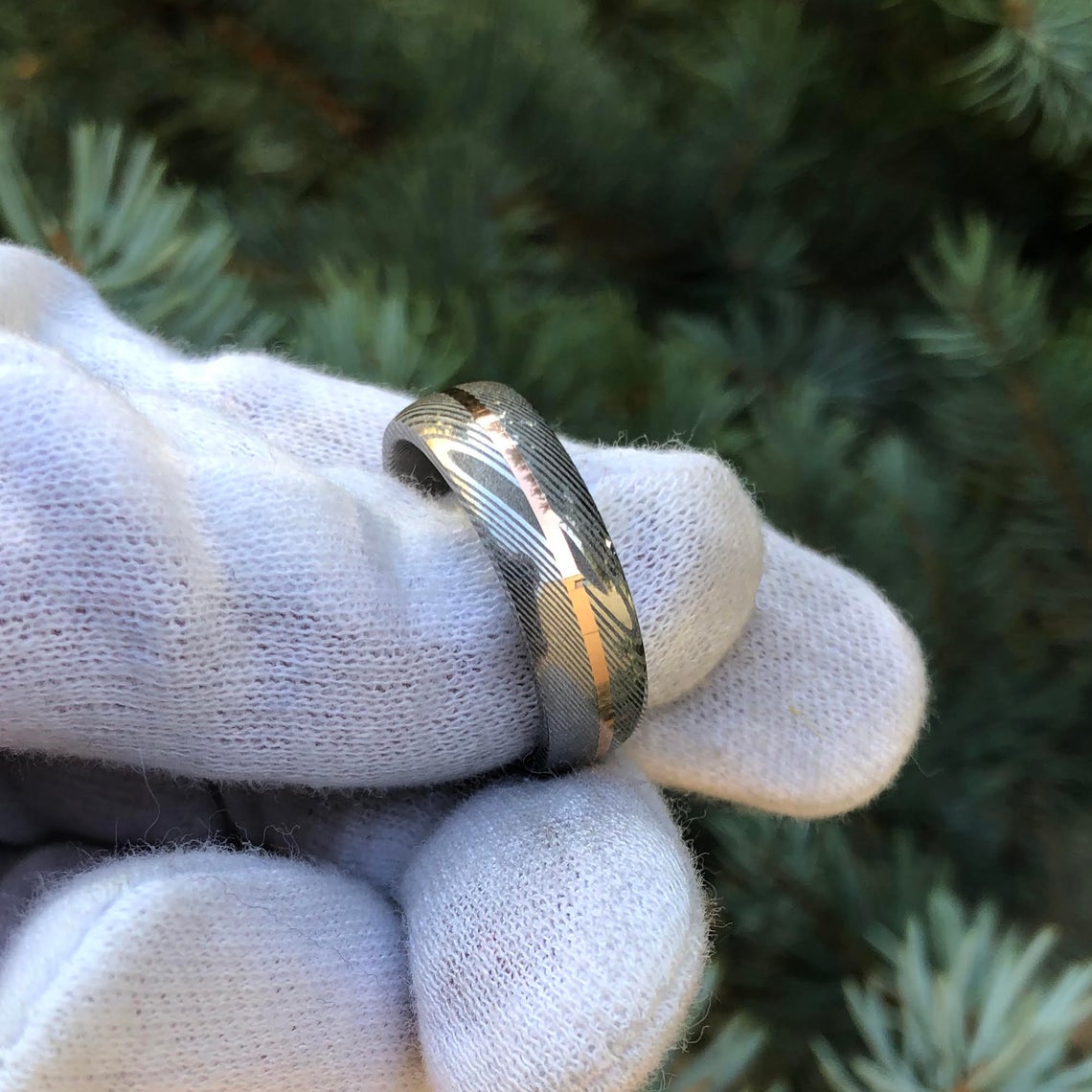 7mm wide white Damascus steel ring with a centered rose gold inlay held by white glove