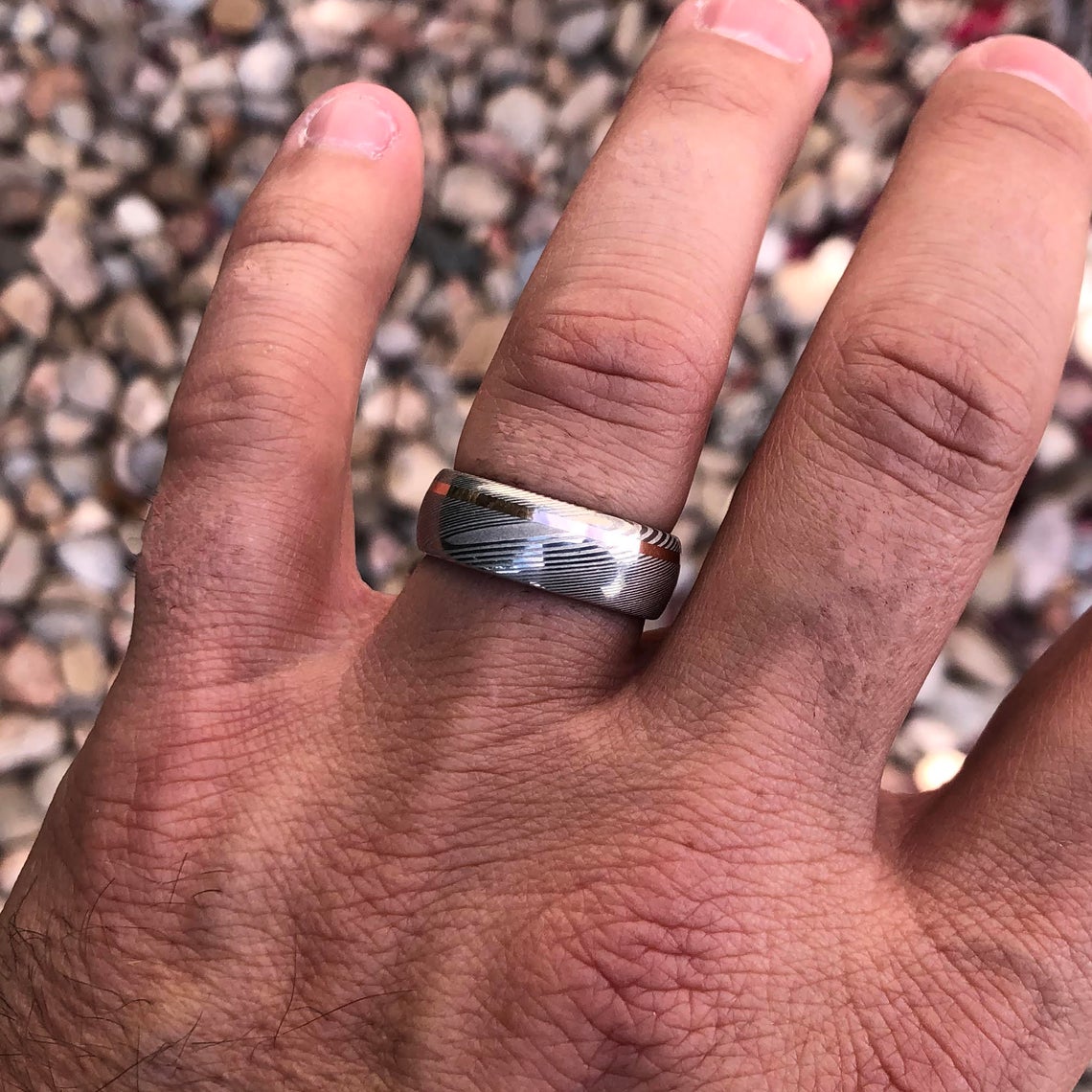 8mm wide white Damascus steel ring with an off-centered rose gold inlay and rounded profile on a man&#39;s hand