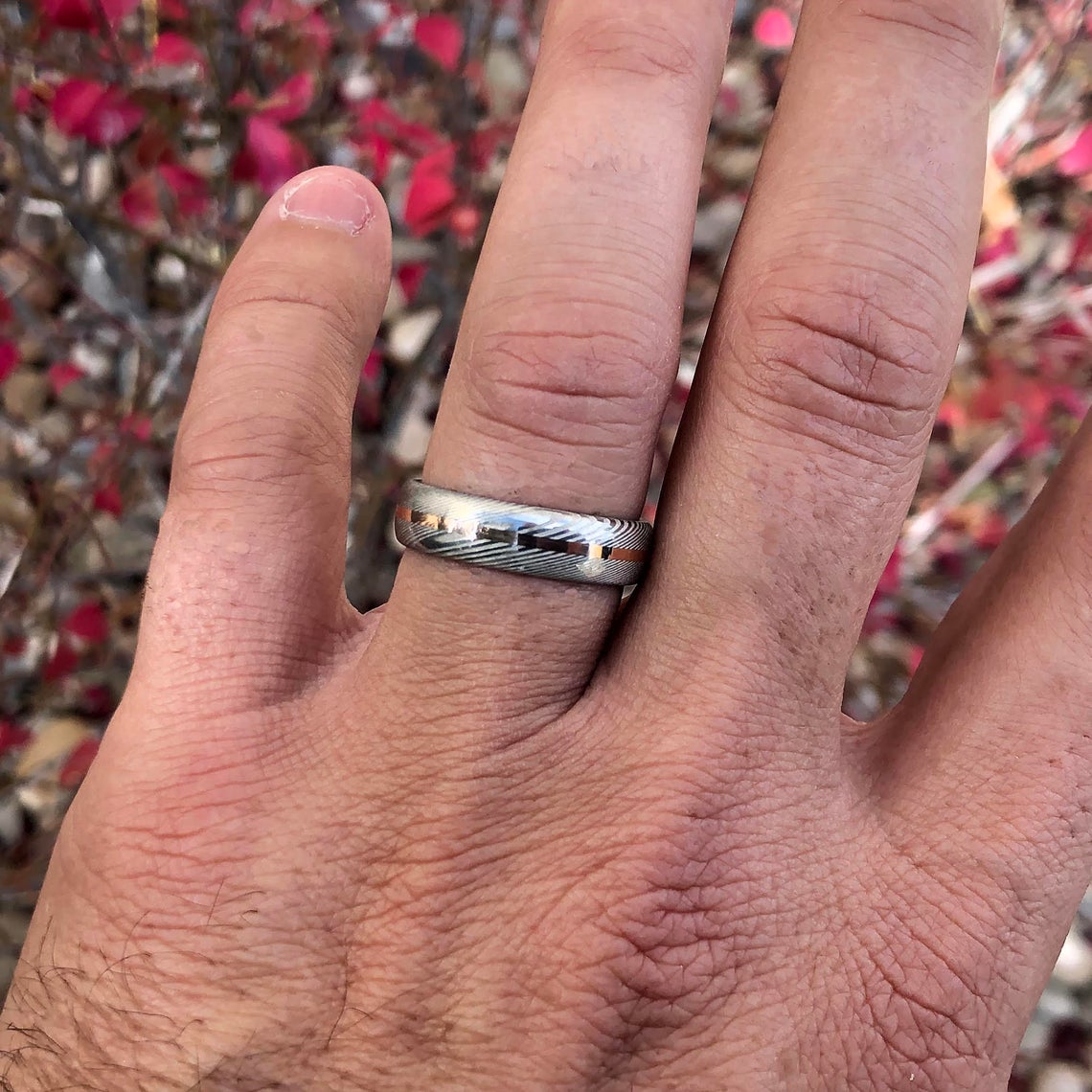 6mm wide Damascus steel wedding band with a centered rose gold inlay on man&#39;s hand