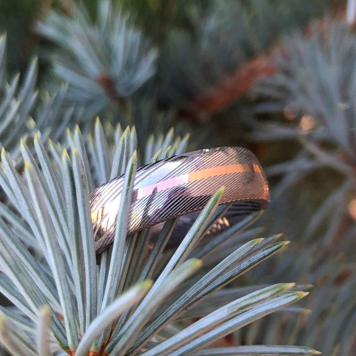 7mm wide white Damascus steel ring with a centered rose gold inlay
