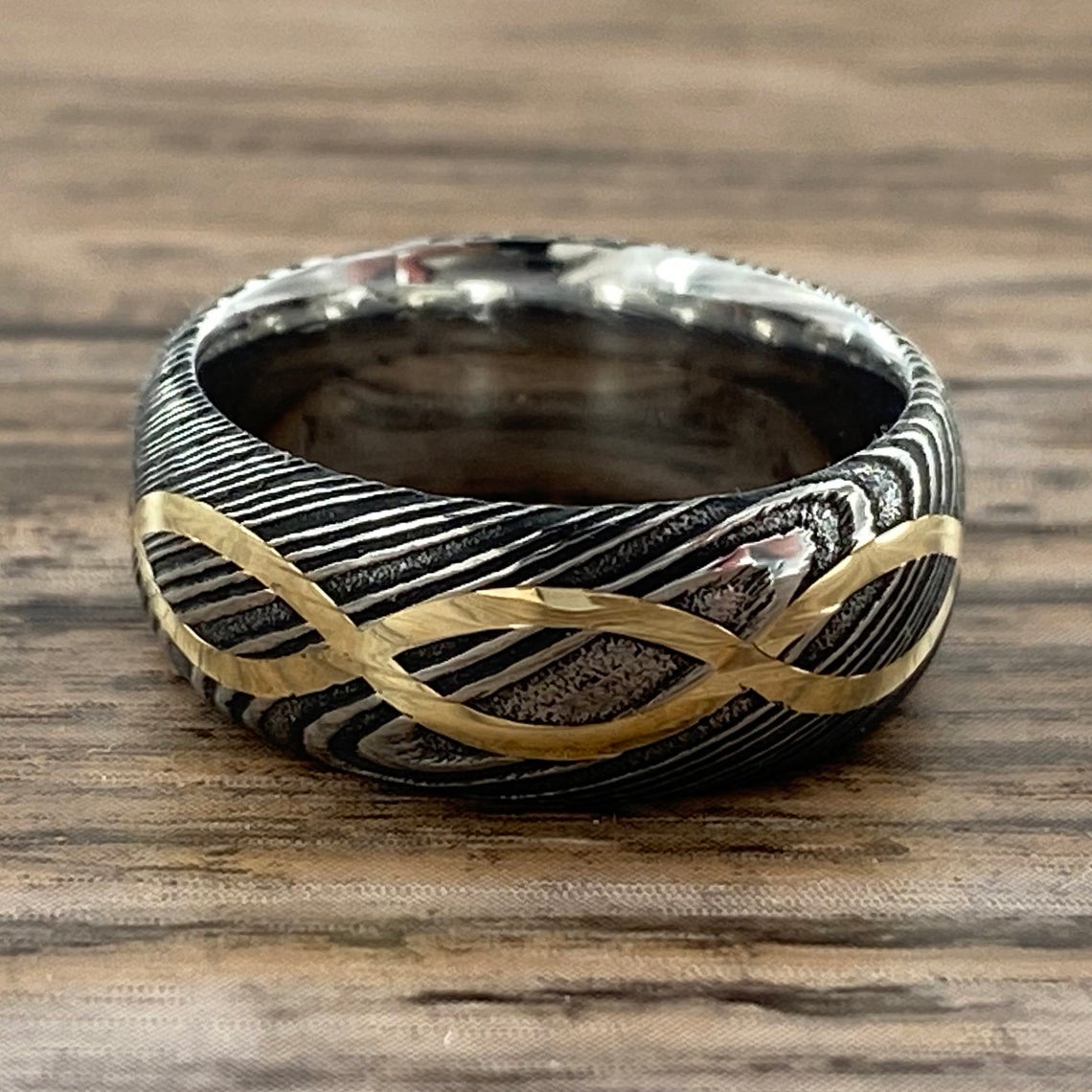 8mm wide Black Damascus steel ring with a 14k yellow gold infinity inlay