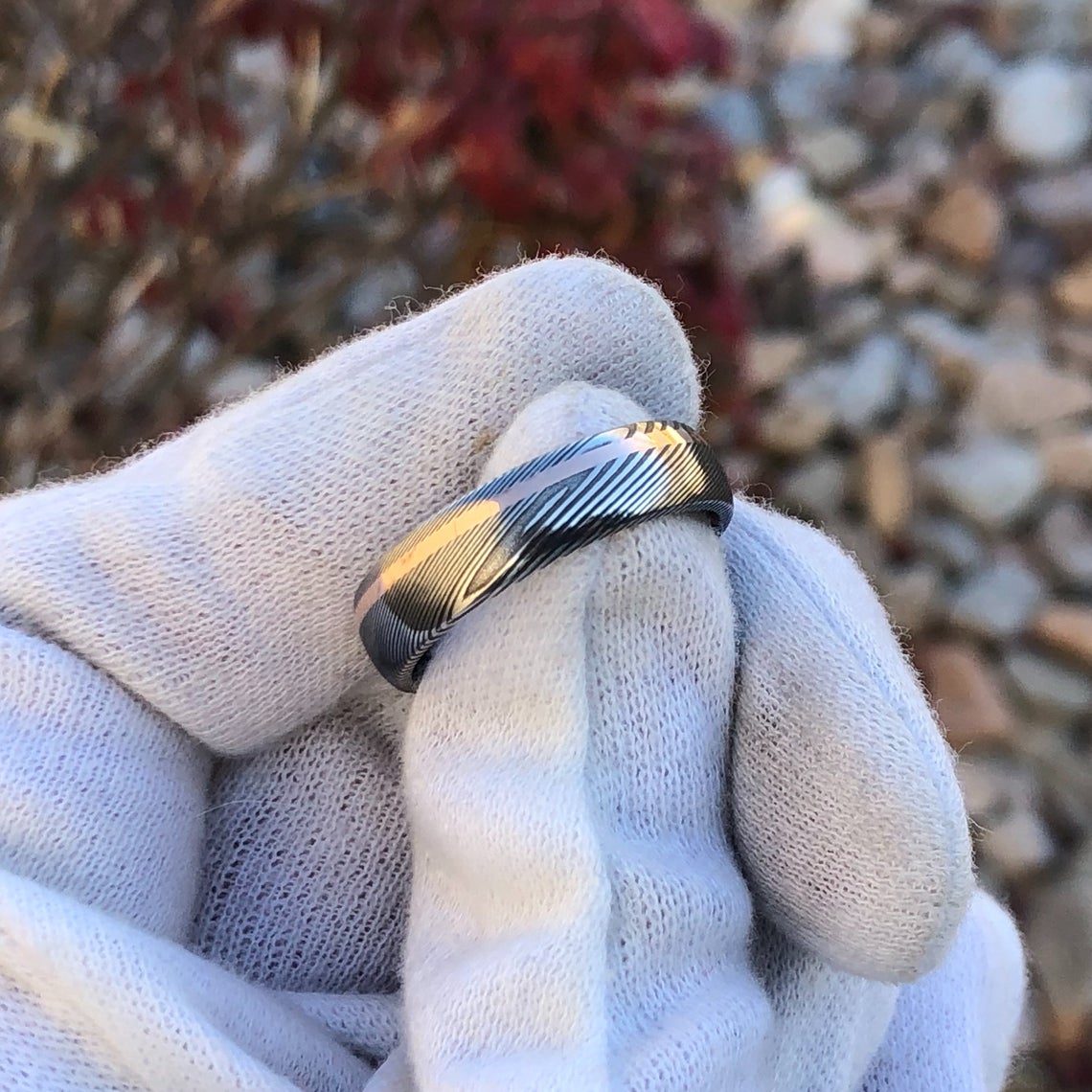 6mm wide Damascus steel ring with an off-centered rose gold inlay held by white glove