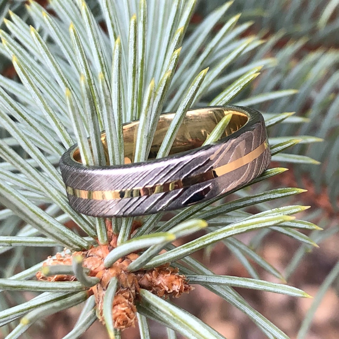 6mm wide white Damascus steel wedding band with a centered yellow gold inlay with a 14k yellow gold sleeve