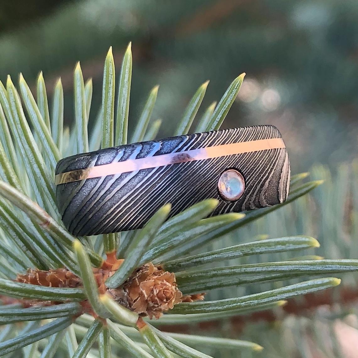 8mm wide black Damascus steel wedding band with an off-centered rose gold inlay with a 3mm round diamond